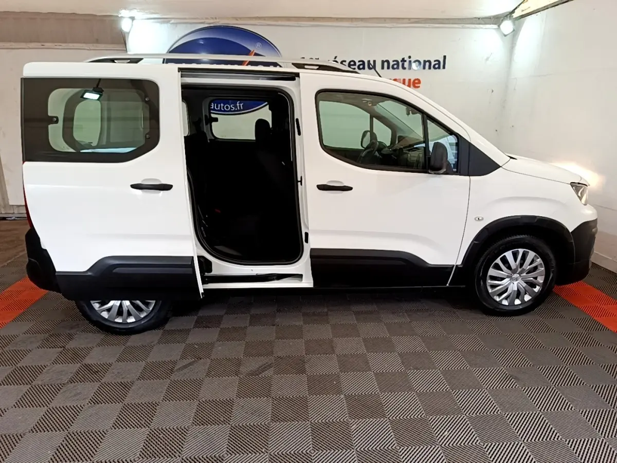 Vue de profil côté droit d'un Peugeot Rifter blanc 2019 avec porte coulissante arrière ouverte, intérieur sombre visible.