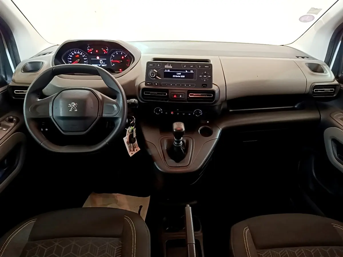 Vue intérieure avant du Peugeot Rifter blanc 2019, tableau de bord noir avec volant, levier de vitesse manuel et écran central.