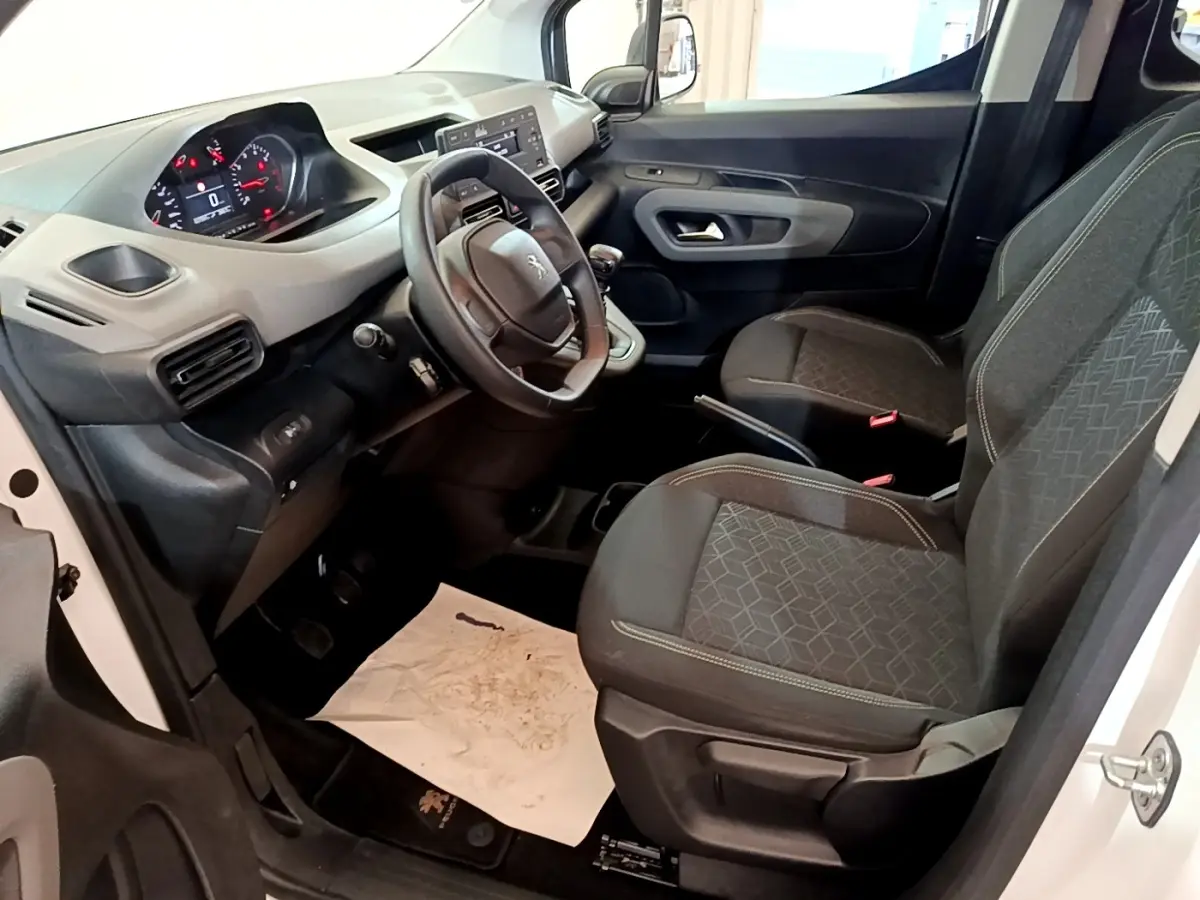 Vue intérieure côté conducteur du Peugeot Rifter blanc 2019, montrant le tableau de bord et les sièges avant en tissu gris.