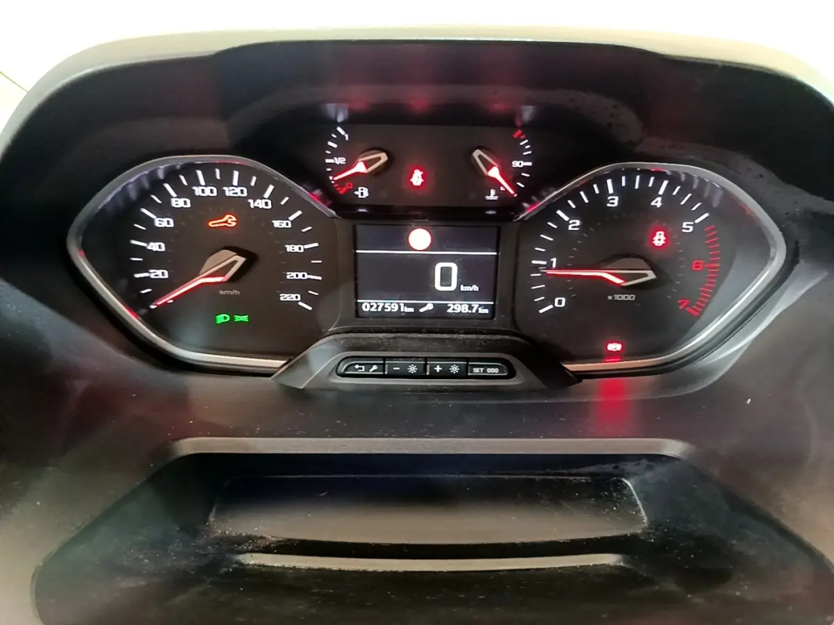 Vue rapprochée du tableau de bord numérique du Peugeot Rifter blanc, affichant la vitesse à 0 km/h et divers voyants allumés.