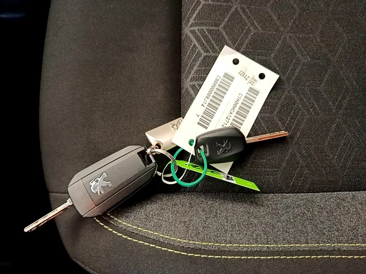 Jeu de clés Peugeot posé sur un siège tissu noir avec surpiqûres jaunes, sans vue directe du véhicule.