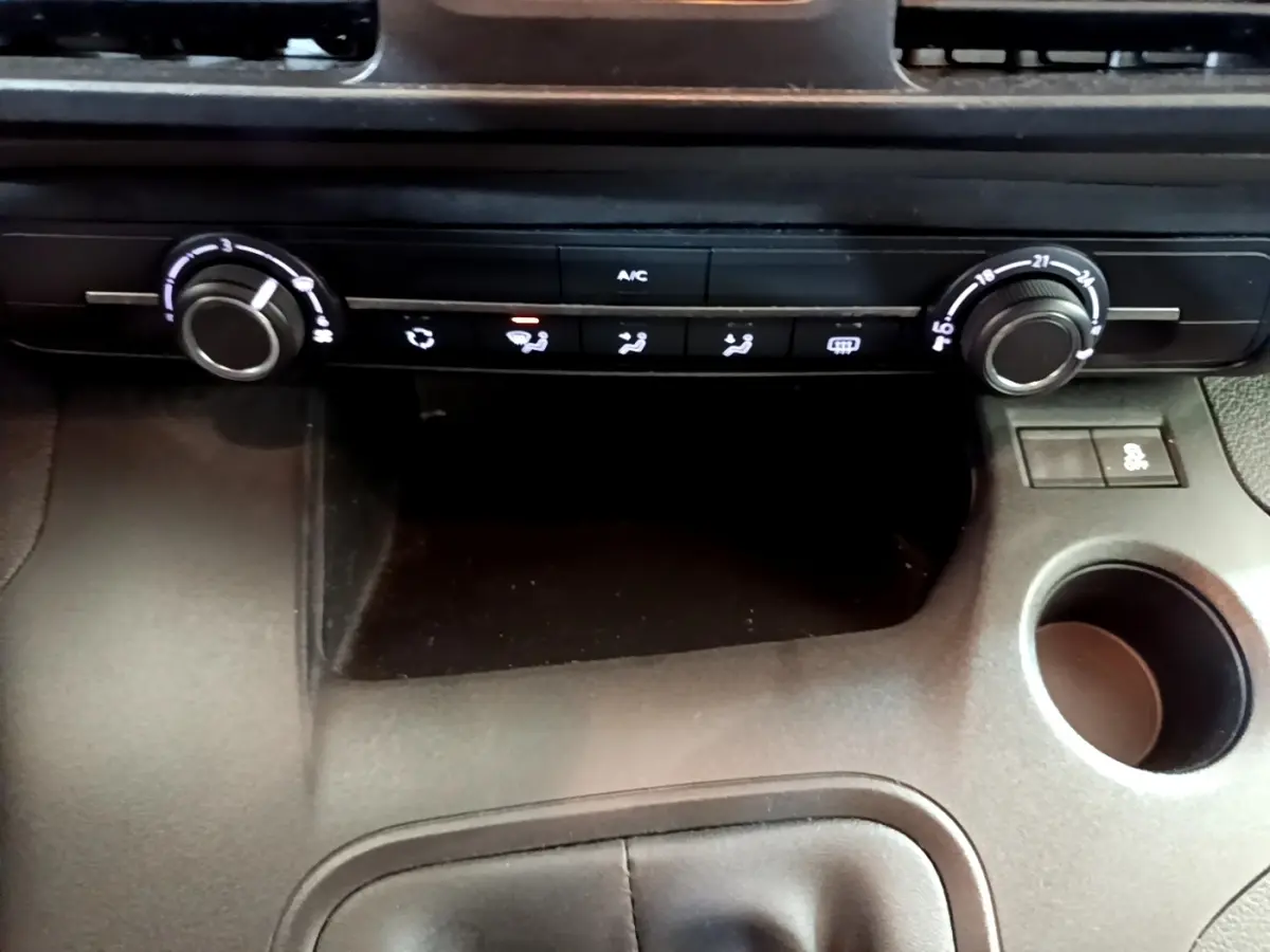 Vue rapprochée de la console centrale du Peugeot Rifter blanc, montrant les commandes de climatisation et un porte-gobelet.