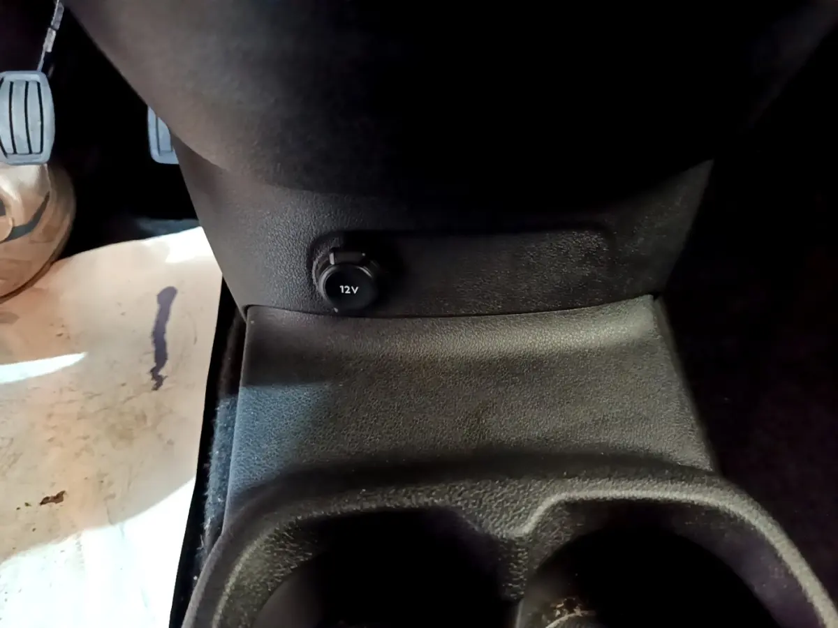 Prise 12V en gros plan sur la console centrale avant du Peugeot Rifter blanc, côté conducteur.