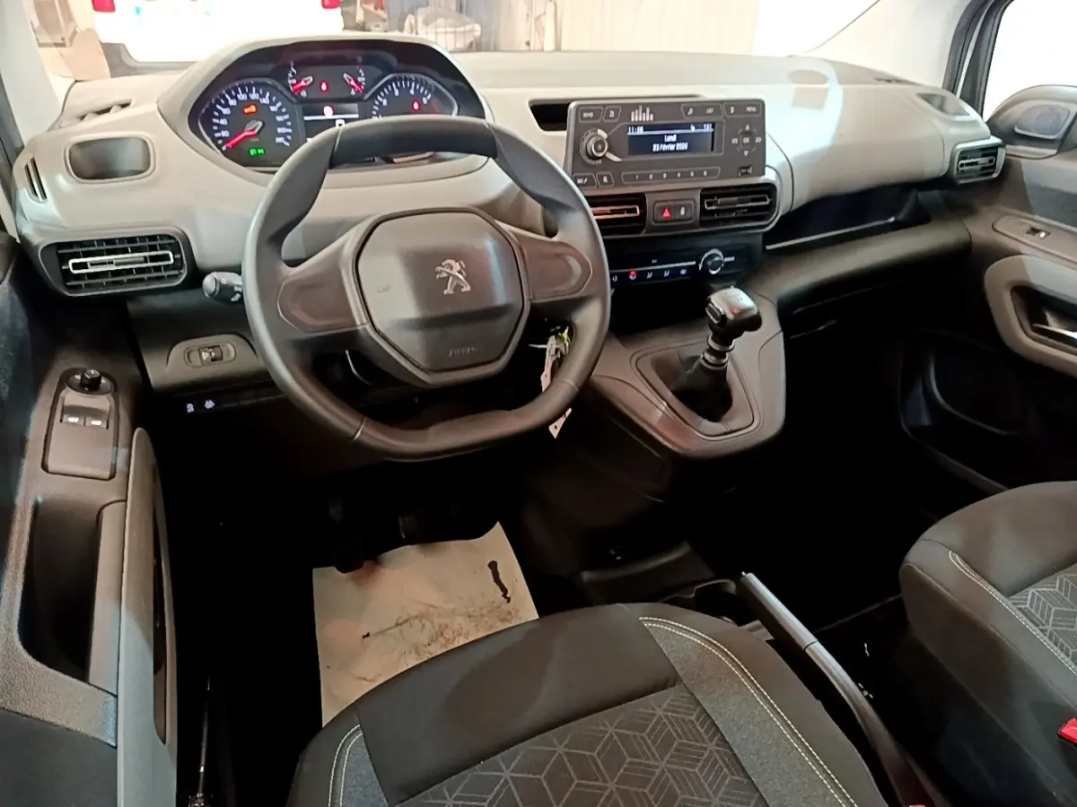 Vue intérieure avant du Peugeot Rifter blanc 2019, volant, tableau de bord numérique et levier de vitesse manuel visibles.