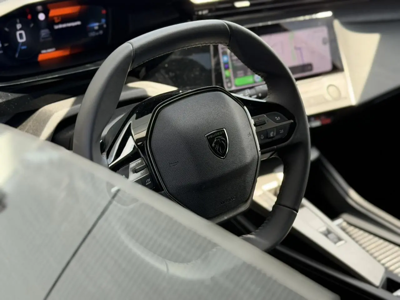 Vue rapprochée du volant cuir noir avec logo Peugeot, tableau de bord digital et écran tactile du Peugeot 308 SW 2025.