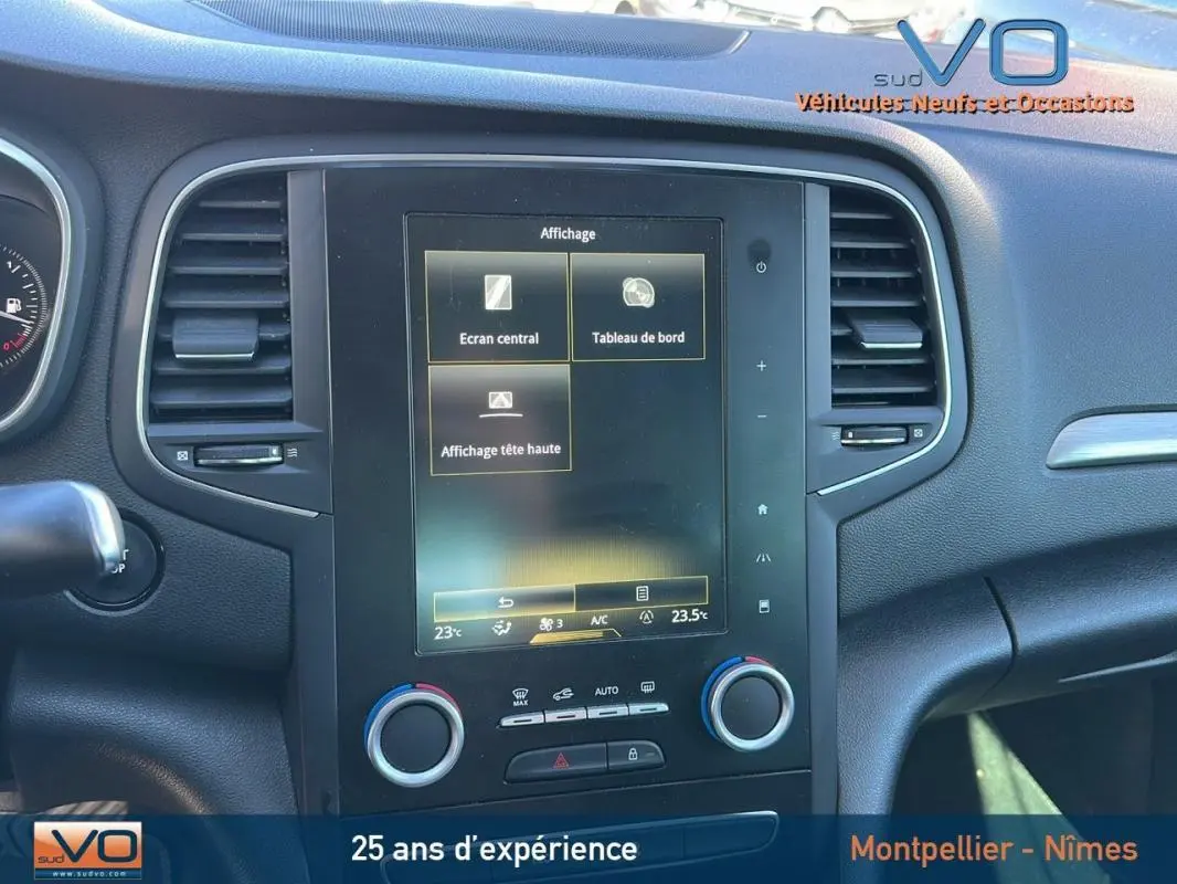 Vue rapprochée de la console centrale noire de la Renault Mégane IV beige, affichant l'écran tactile et commandes climatisation.