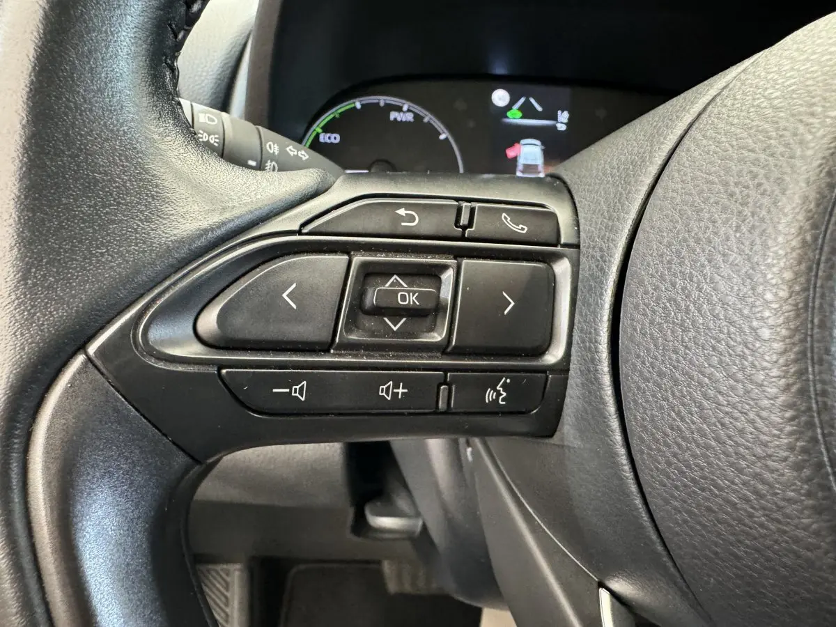Gros plan sur les commandes gauche du volant cuir noir de la Toyota Yaris Hybride 2022 avec affichage digital en arrière-plan.