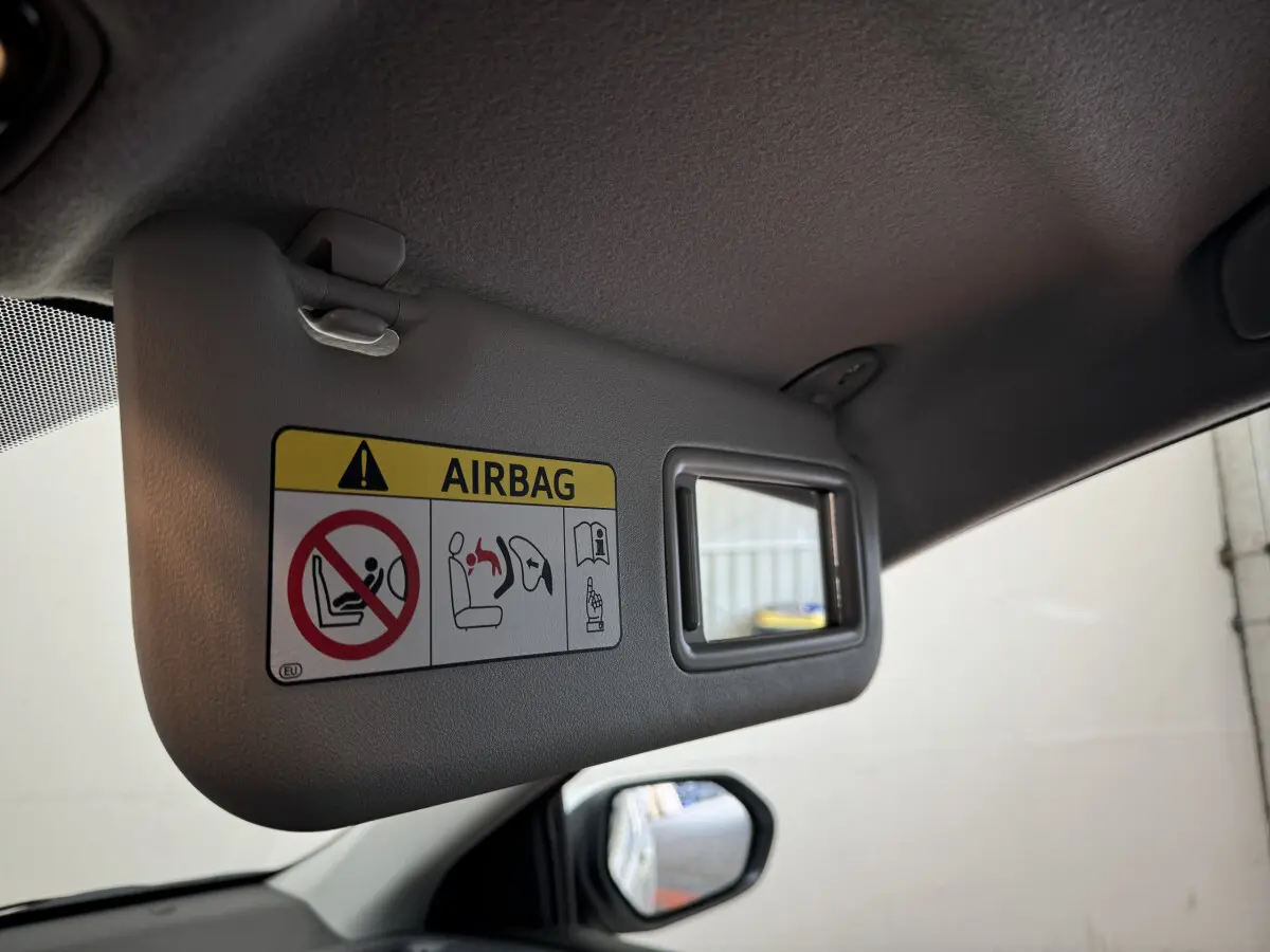 Détail du pare-soleil côté conducteur gris avec avertissement airbag et miroir intégré dans une Toyota Yaris blanche 2022.