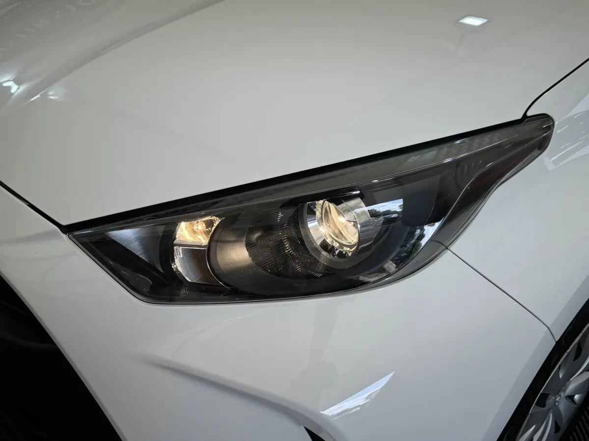 Gros plan sur le phare avant droit allumé d'une Toyota Yaris hybride blanche 2022, avec carrosserie lisse et jante visible.