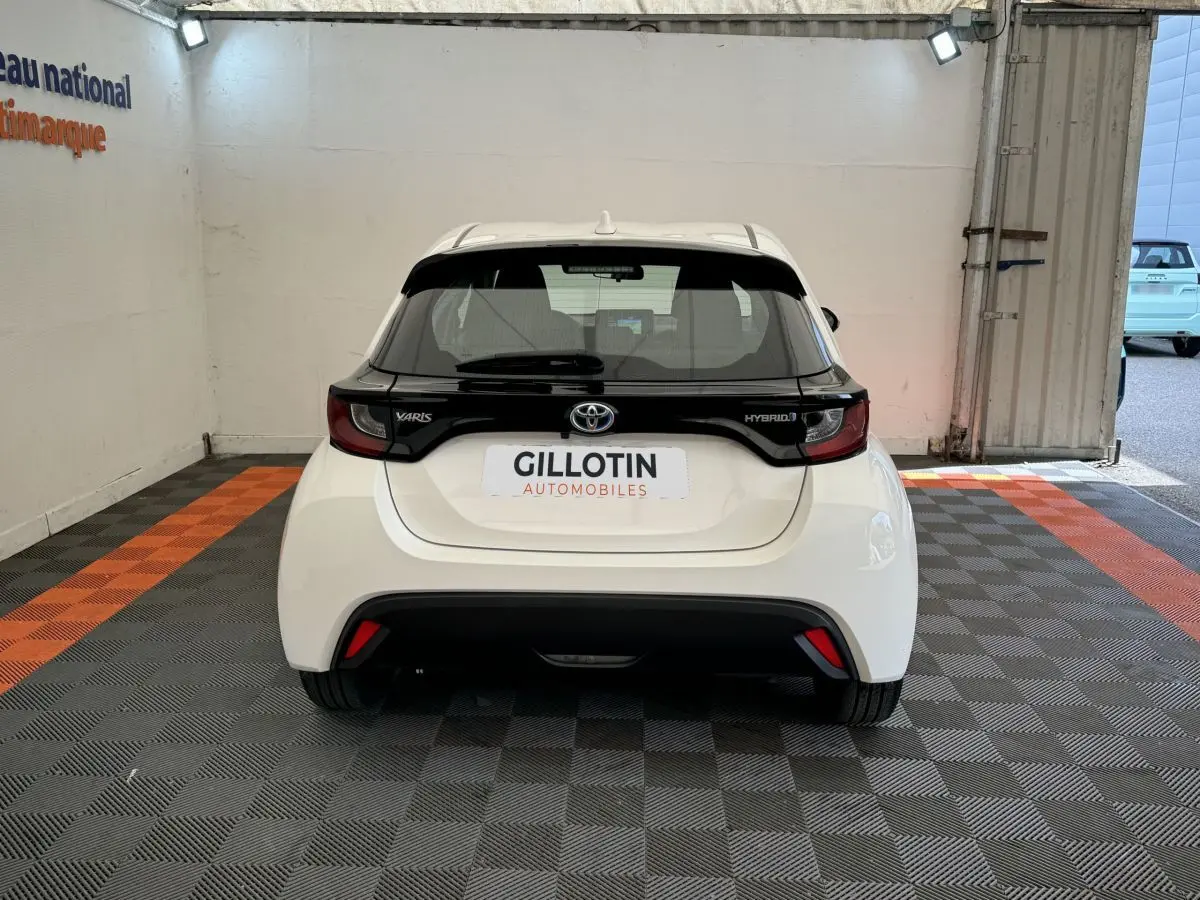 Vue arrière d'une Toyota Yaris hybride blanche avec bande noire distinctive sur le hayon et feux arrière intégrés.