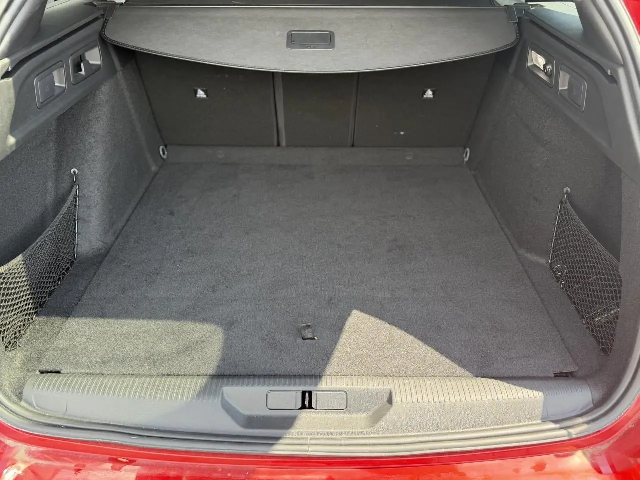 Coffre ouvert vu de l'arrière d'une Peugeot 308 SW Rouge Elixir, avec tapis de sol et filet de rangement latéral.