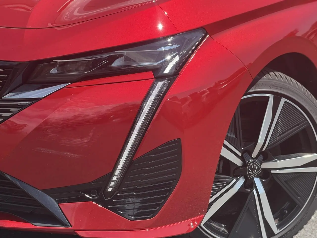 Gros plan sur l'avant droit rouge Elixir du Peugeot 308 SW 2024, mettant en valeur le phare LED et la jante alliage 18''.