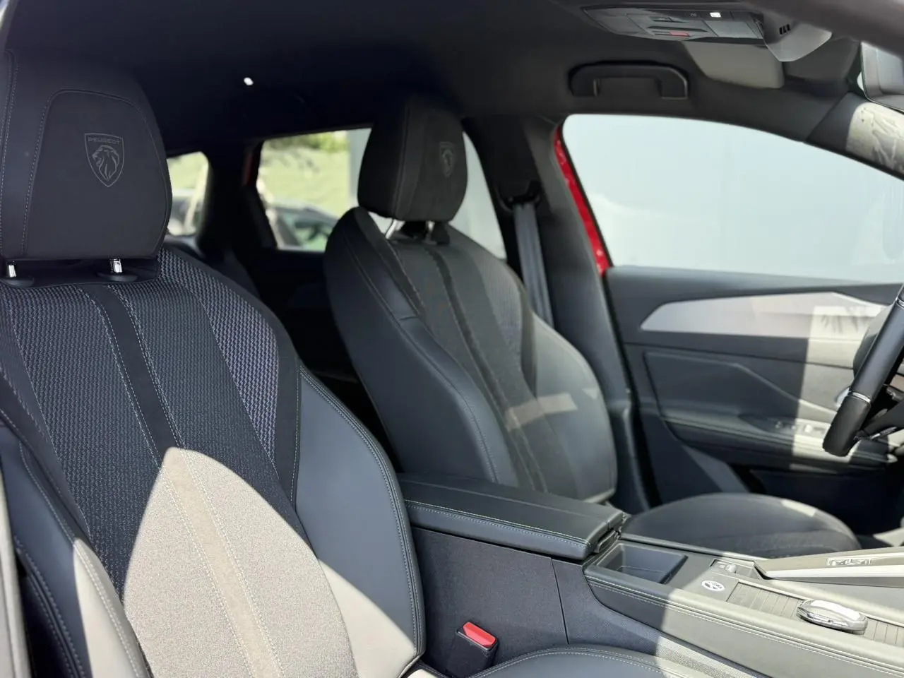 Vue intérieure côté conducteur montrant les sièges avant noirs avec logo Peugeot brodé sur les appuie-têtes.