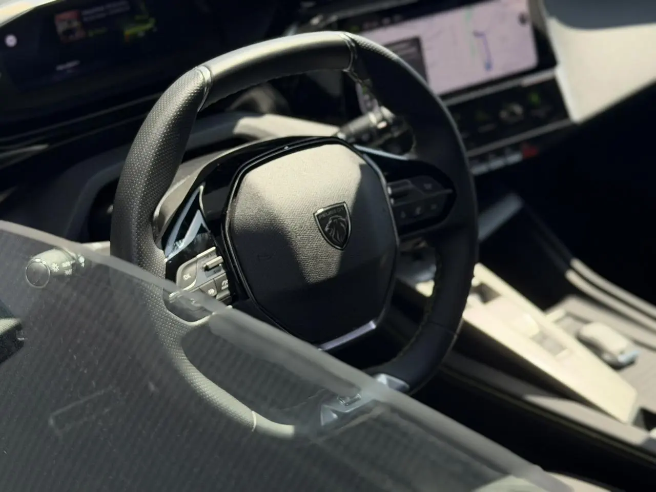 Gros plan sur le volant cuir noir du Peugeot 308 SW 2024 avec tableau de bord numérique et console centrale beige.