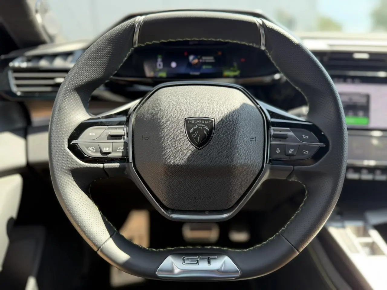 Volant cuir noir au design compact avec logo Peugeot et badge GT, vue frontale centrée sur le poste de conduite.