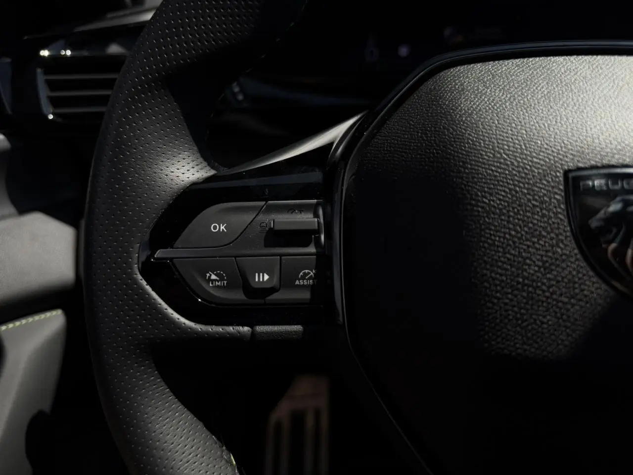 Gros plan sur le volant cuir perforé de la Peugeot 308 SW 2024 avec commandes intégrées et logo Peugeot visible.