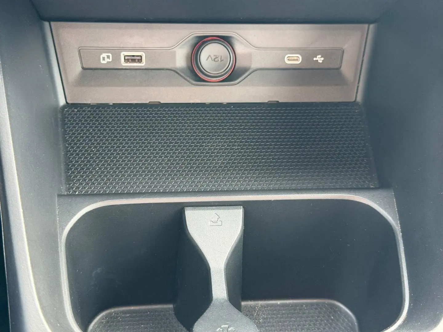 Gros plan sur la console centrale noire du MG3 1.5 Hybrid+ avec prise 12V, port USB et rangement intégré.