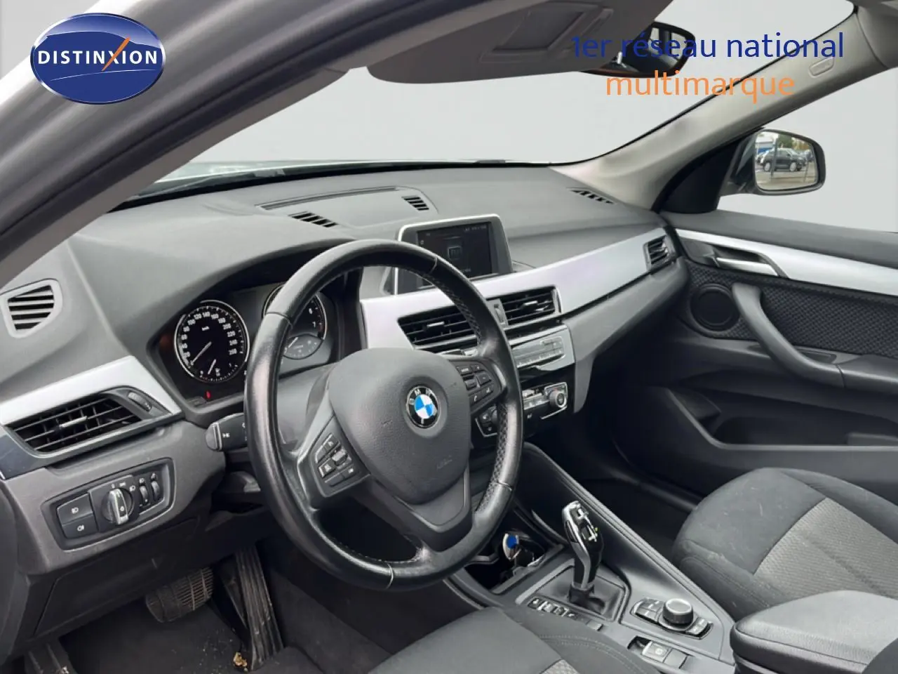 Vue intérieure côté conducteur du tableau de bord et volant d'une BMW X1 18i gris argent de 2018.