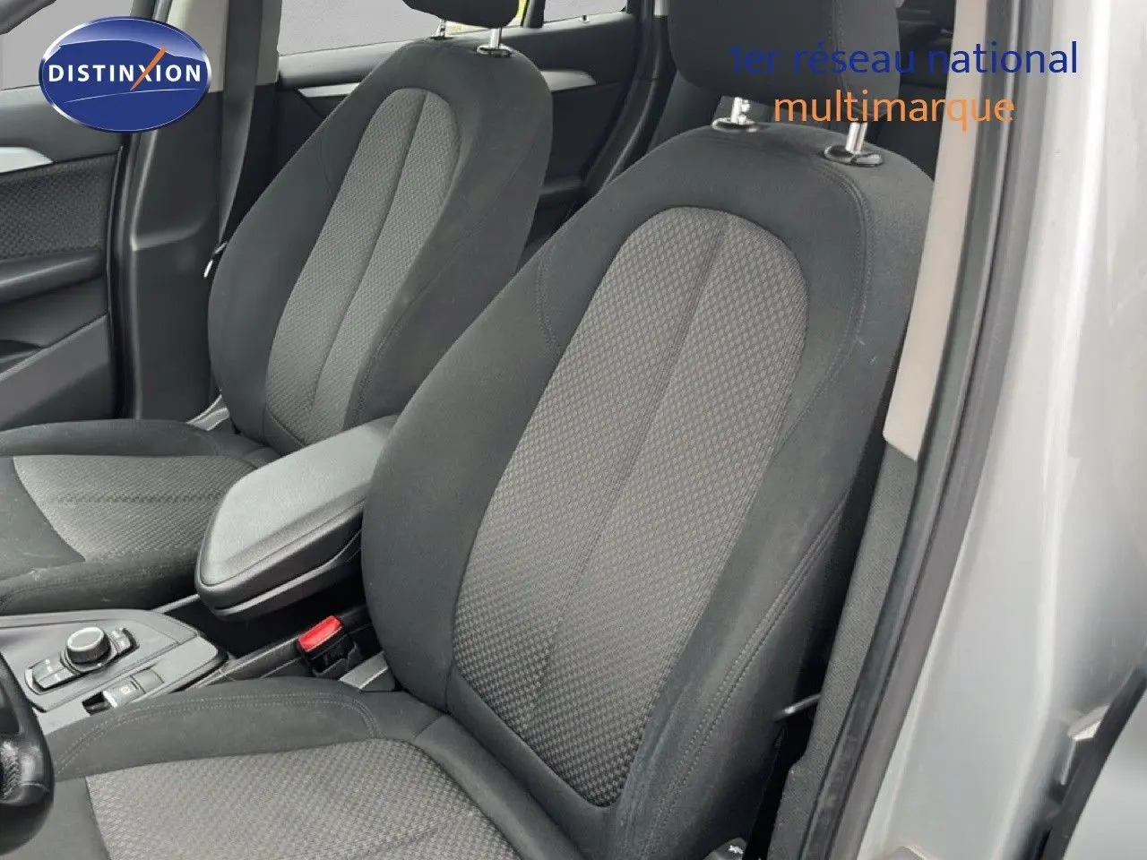 Vue intérieure rapprochée des sièges avant en tissu gris noir d’une BMW X1 18i gris argent 2018, porte ouverte côté droit.