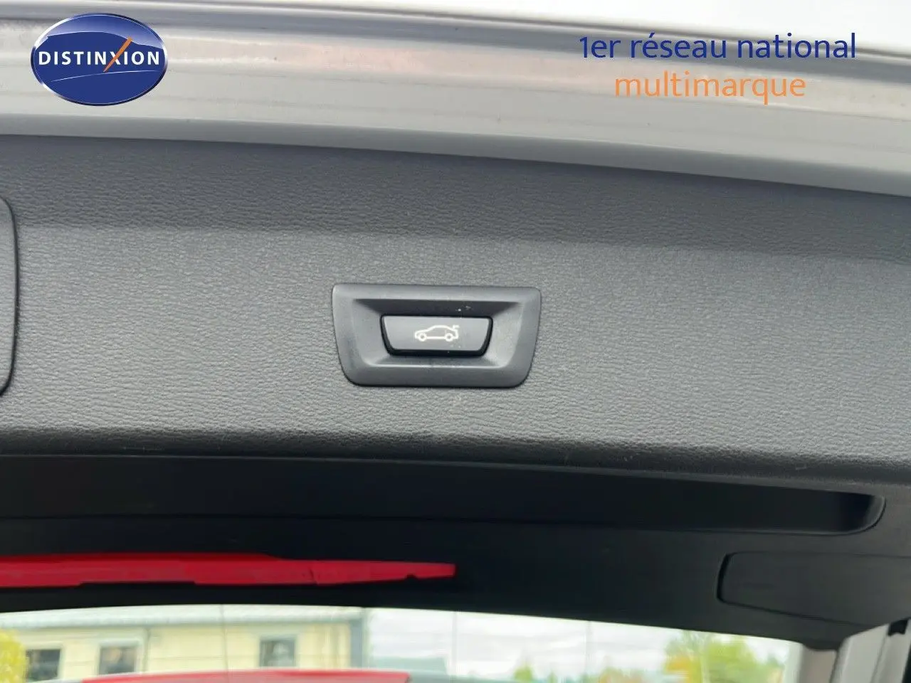 Détail du bouton d'ouverture électrique du coffre sur la partie intérieure du hayon d'un BMW X1 gris argent.