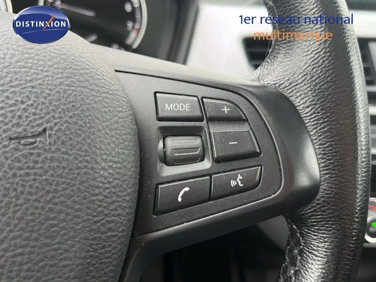 Gros plan sur les commandes du volant en cuir noir du BMW X1 18i gris argent, mettant en valeur les boutons multifonctions.