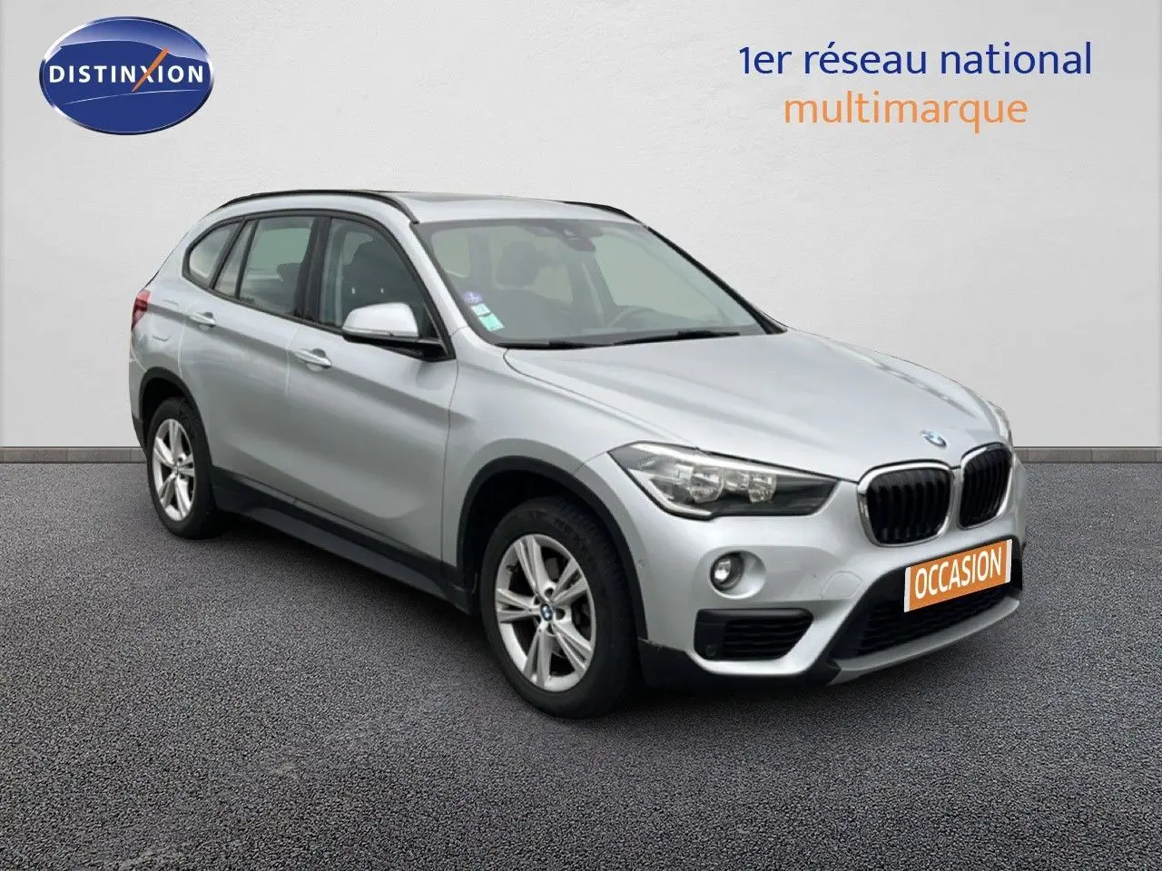 BMW X1 18i gris argent métal en 3/4 avant droit, avec calandre noire et jantes alliage 17 pouces.
