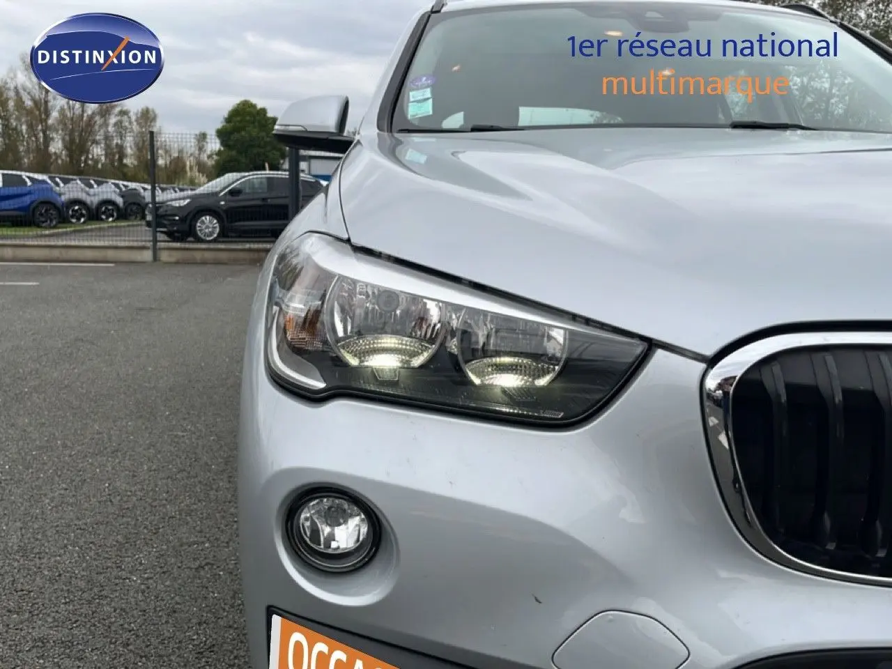 Vue avant gauche rapprochée d’un BMW X1 gris argent métallisé avec phares allumés et calandre noire distinctive.
