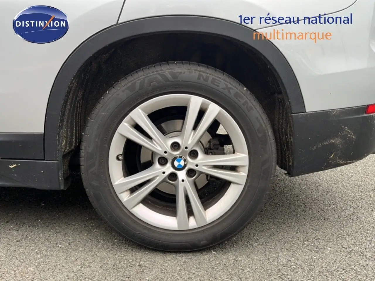 Gros plan sur la roue arrière droite d’un BMW X1 gris argent métallisé, avec jante alu 17 pouces et logo BMW visible.