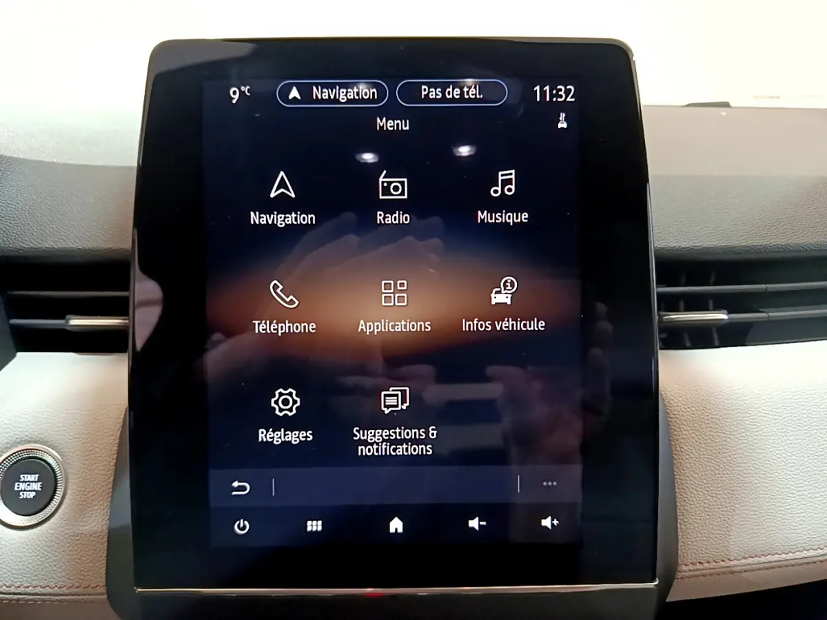 Écran tactile central allumé avec menu principal dans l'habitacle clair d'une Renault Clio Initiale Paris E-TECH 140 orange.