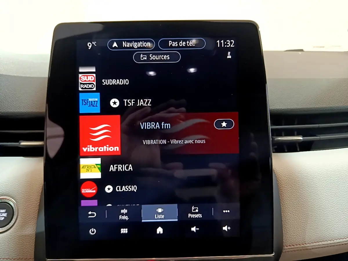 Écran tactile central affichant les stations radio dans l'habitacle clair d'une Renault Clio Initiale Paris E-TECH 2021