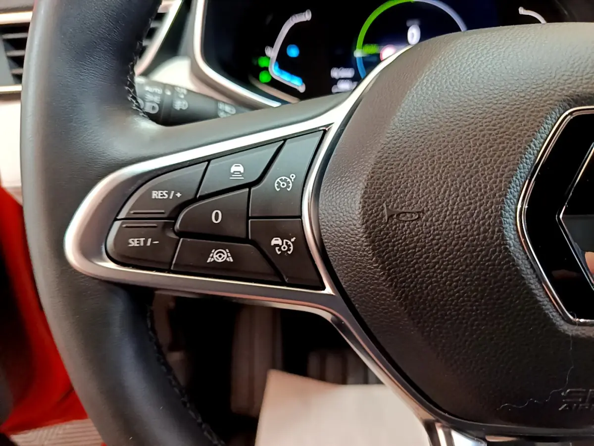 Gros plan sur le volant cuir noir de la Renault Clio Initiale Paris orange, avec commandes de régulateur de vitesse visibles à gauche.