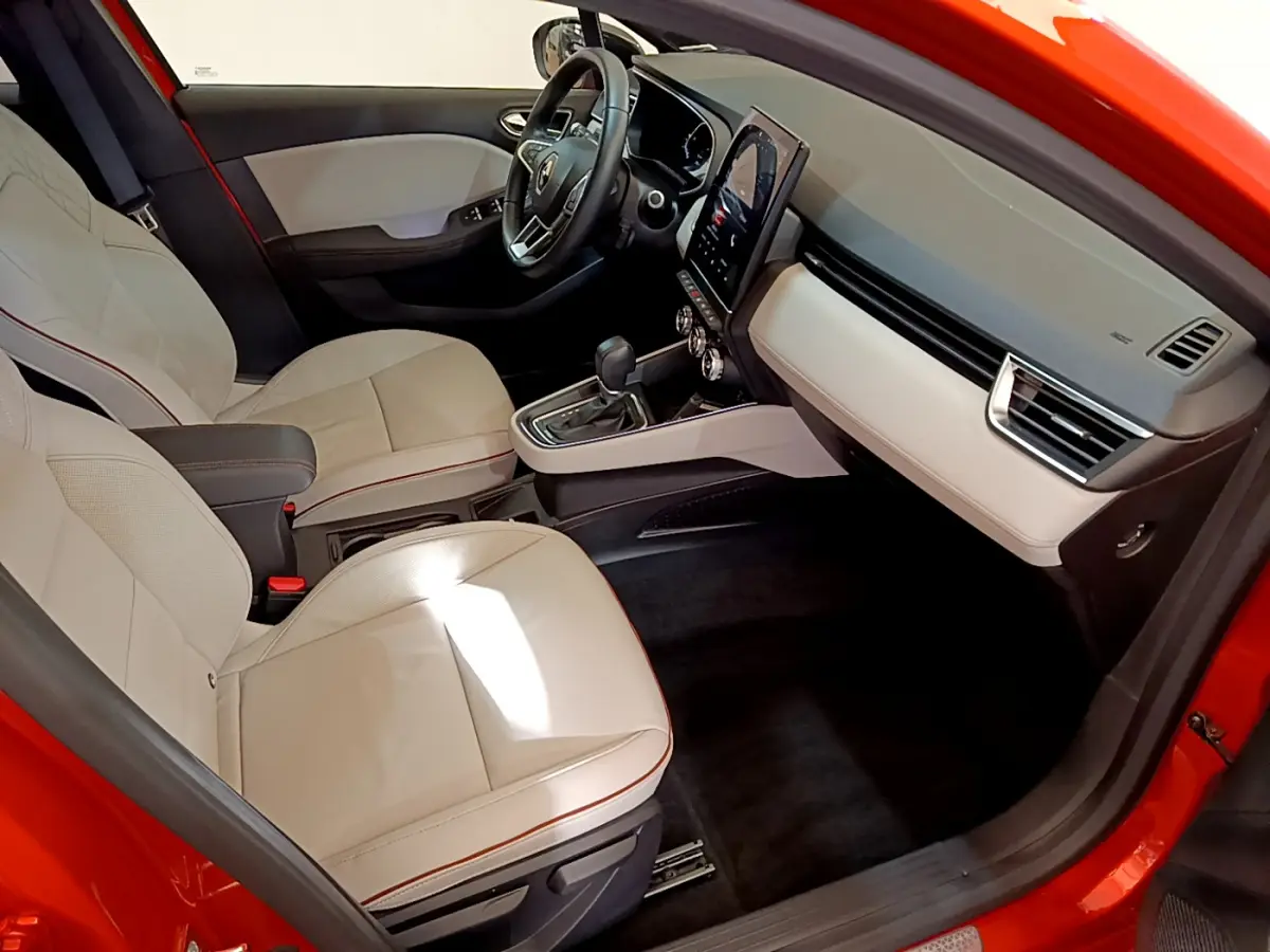 Intérieur côté conducteur d'une Renault Clio Initiale Paris orange, sièges clairs et tableau de bord moderne avec écran tactile vertical.