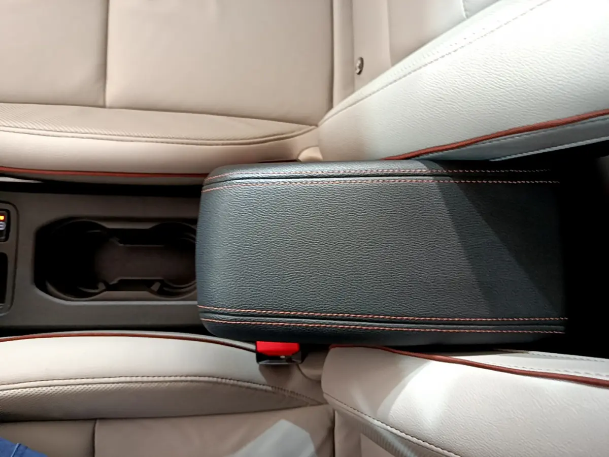 Vue rapprochée de l'accoudoir central noir avec surpiqûres orange et sièges cuir beige de la Renault Clio Initiale Paris E-TECH 2021.