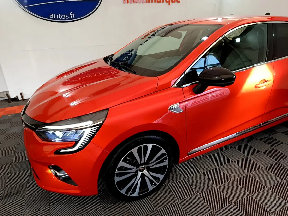 Renault Clio Initiale Paris orange vue 3/4 avant droit avec phares LED allumés et jantes distinctives.