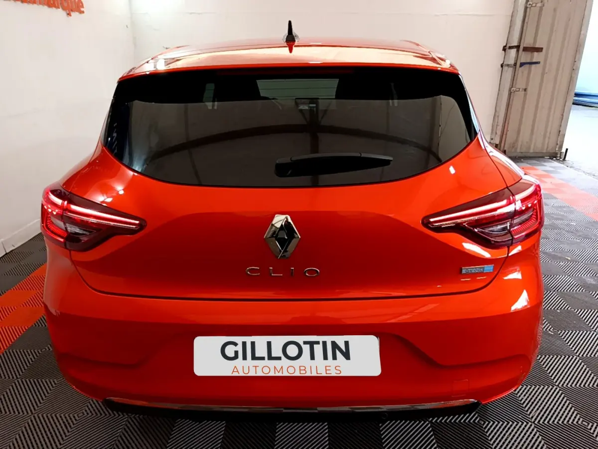 Vue arrière d'une Renault Clio Initiale Paris E-TECH 140 orange vif avec feux LED et logo distinctif Renault.