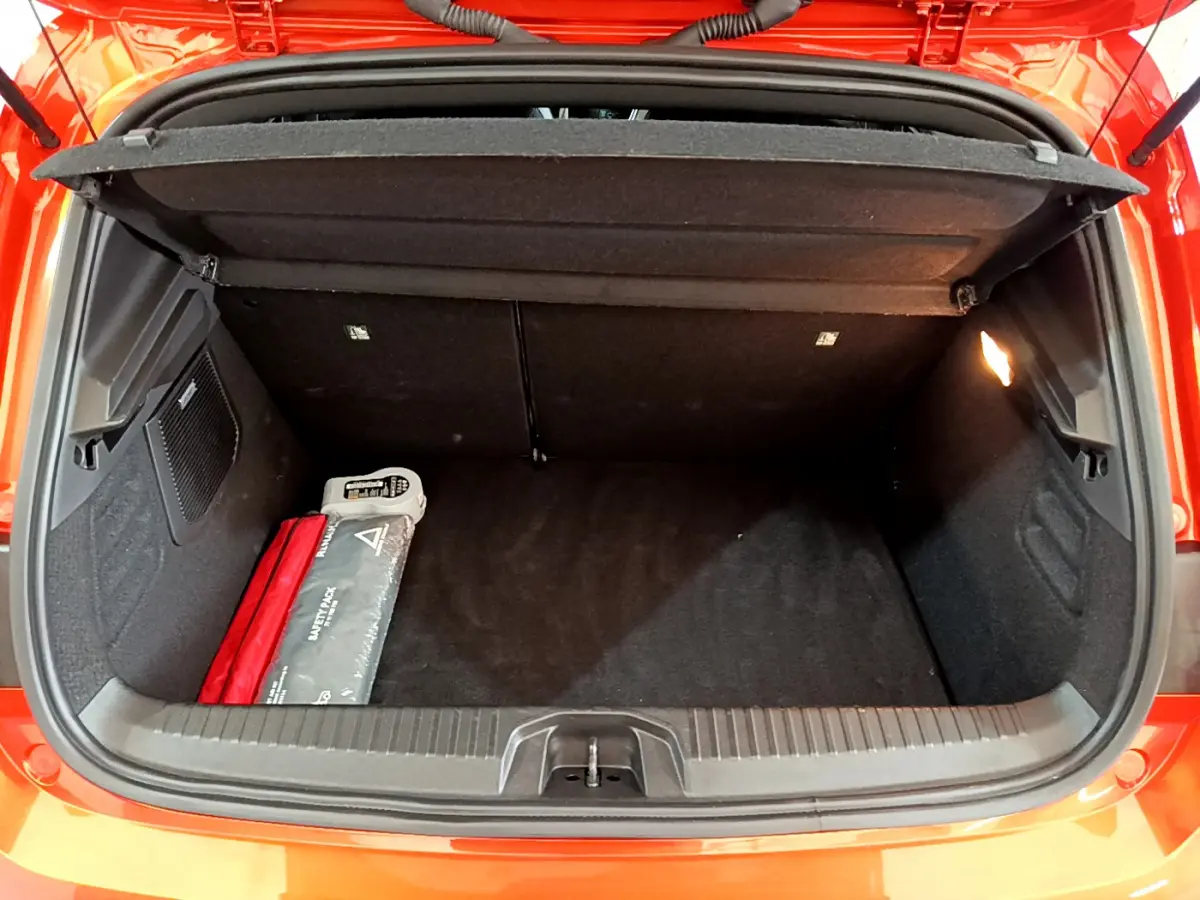 Coffre ouvert vu de l'arrière d'une Renault Clio Initiale Paris orange, avec trousse de sécurité visible à gauche.