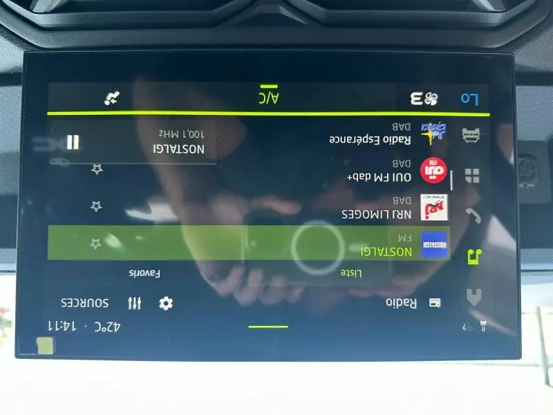 Écran tactile central du tableau de bord du Dacia Duster blanc, affichant la liste des radios FM.