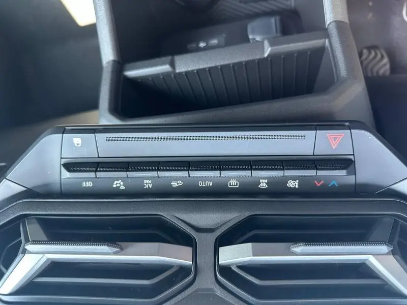 Vue rapprochée du tableau de bord du Dacia Duster blanc 2025, montrant les commandes de climatisation et les aérateurs noirs.