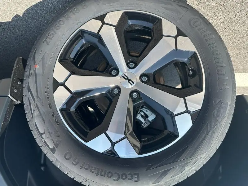 Gros plan sur la jante alu bicolore noire et argentée d'un Dacia Duster blanc, mettant en valeur le logo central et le pneu Continental.