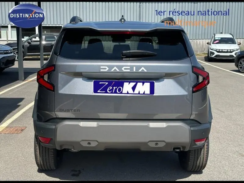 Vue arrière d'un Dacia Duster gris avec feux arrière en forme de C et plaque Zéro KM visible en concession.