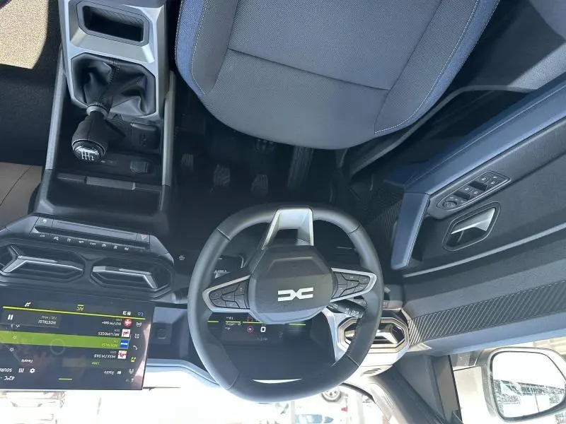 Vue intérieure du poste de conduite du Dacia Duster blanc 2025, volant multifonction et écran tactile visible.