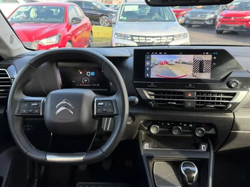 Vue intérieure du tableau de bord et volant d'une Citroën C4 gris 2024 avec écran tactile et caméra de recul affichée.