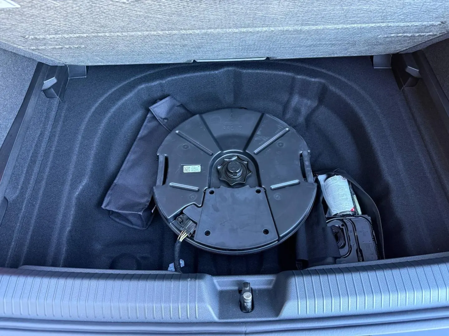 Vue plongeante sur le coffre ouvert d'une Volkswagen Golf noir, montrant la roue de secours et le rangement intérieur.