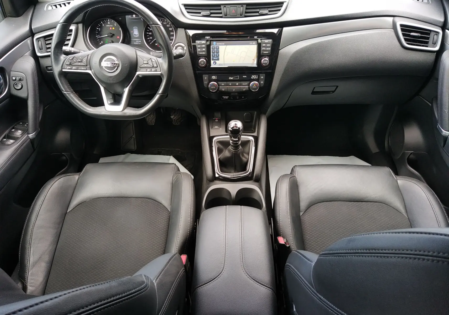 Vue intérieure frontale du Nissan Qashqai 1.2 dig-t 2018, sièges cuir noir, tableau de bord avec écran GPS et boîte manuelle.
