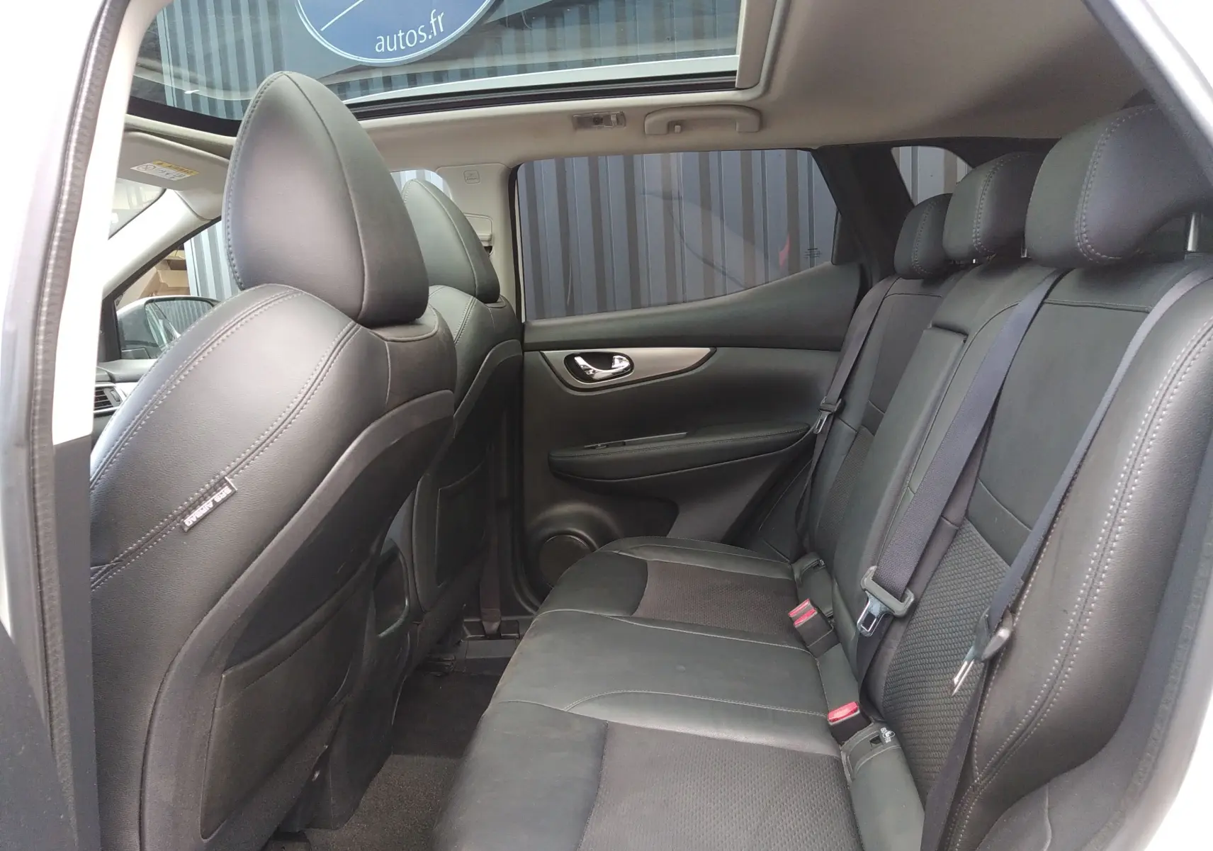 Vue intérieure côté droit montrant les sièges arrière en cuir noir du Nissan Qashqai blanc 2018 avec toit panoramique.