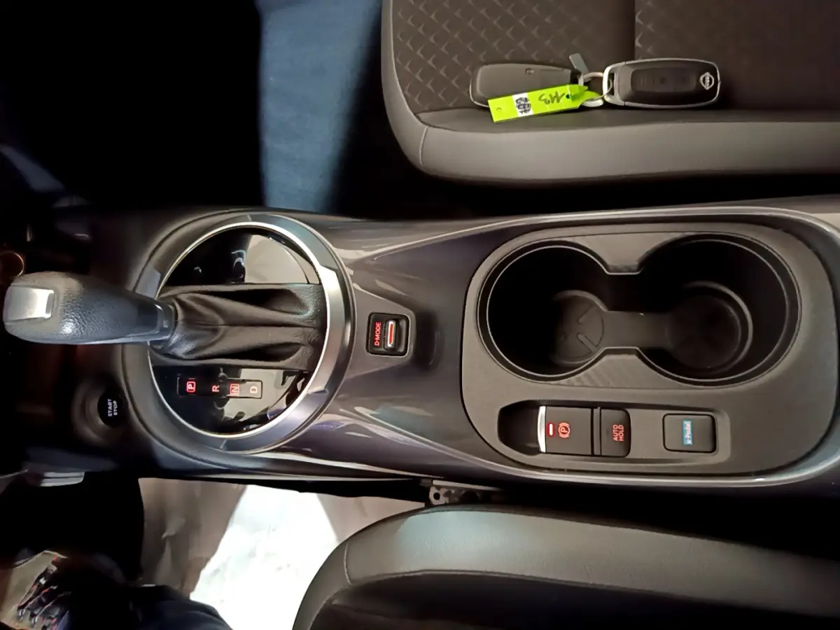 Vue plongeante sur la console centrale grise du Nissan Juke Hybrid 143 Business+ avec levier de vitesses automatique et porte-gobelets.