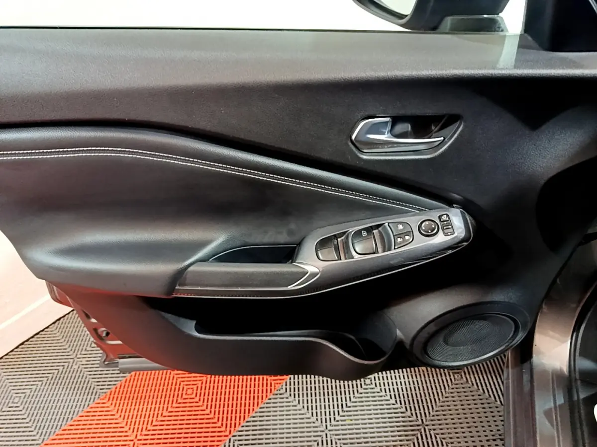 Gros plan sur la porte côté conducteur du Nissan Juke Hybrid gris foncé, montrant les commandes électriques et le haut-parleur intégré.