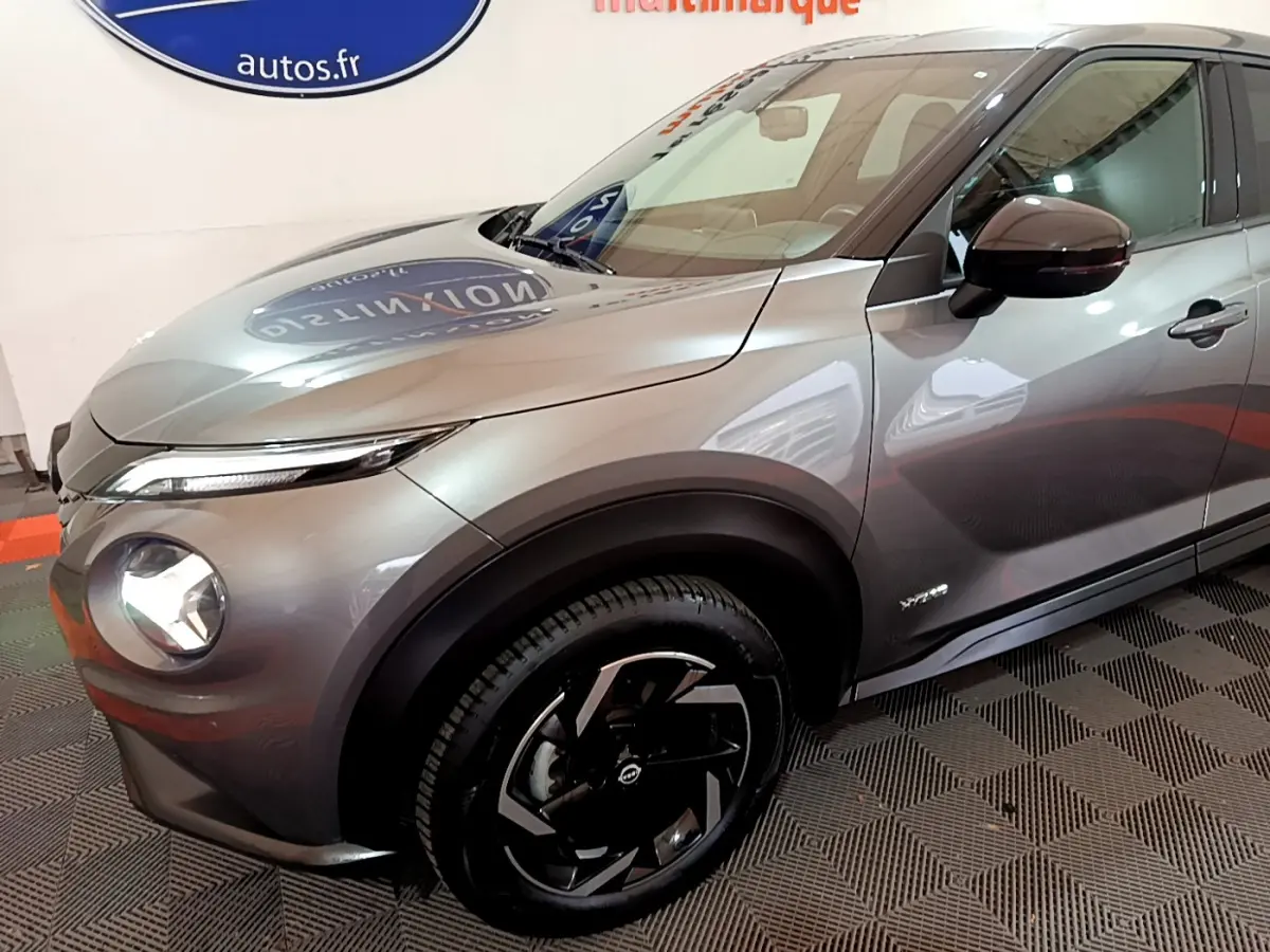 Nissan Juke Hybrid 143 Business+ gris foncé vu en 3/4 avant droit avec jantes noires et phares LED allumés.