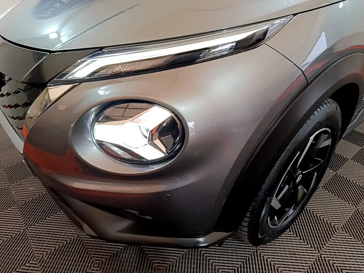 Gros plan sur le phare avant droit et la roue noire d'un Nissan Juke Hybrid gris foncé 2023.