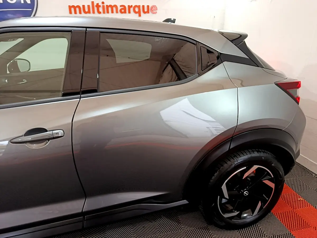Vue latérale gauche du Nissan Juke Hybrid 143 Business+ gris foncé, soulignant la ligne de caisse et la jante noire à motifs géométriques.